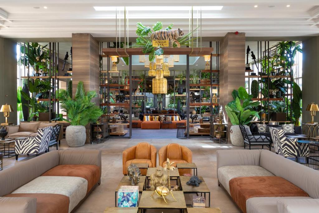 Mūsdienīga viesnīcas uzgaidāmā telpa ar zaļiem augiem, stilīgām mēbelēm un dekoratīviem elementiem, radot relaksējošu atmosfēru. Izcila dizaina un komforta kombinācija.