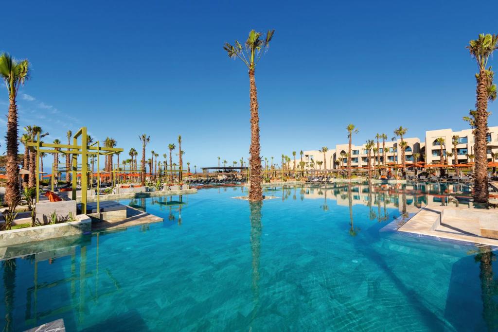 Luksusa kūrorts ar lielu baseinu, palmām un skaidru zilo debesi, radot relaksējošu atmosfēru. Ideāla vieta atpūtai un izklaidei.
