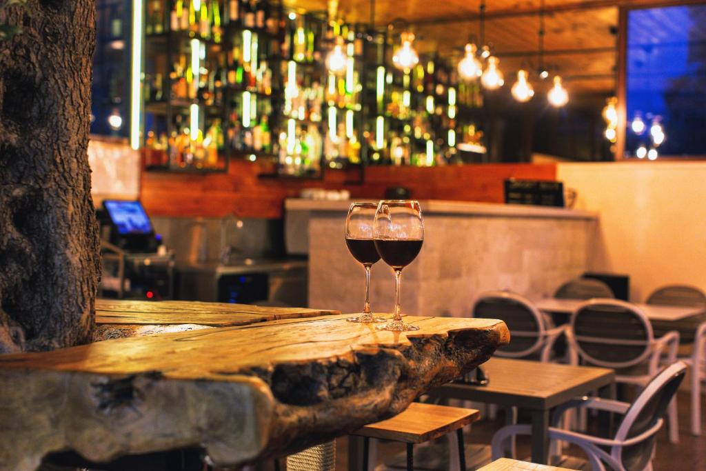 Elegants restorāns ar divām glāzēm sarkanvīna uz koka galda, fons ar modernu bāru un apgaismojumu.
