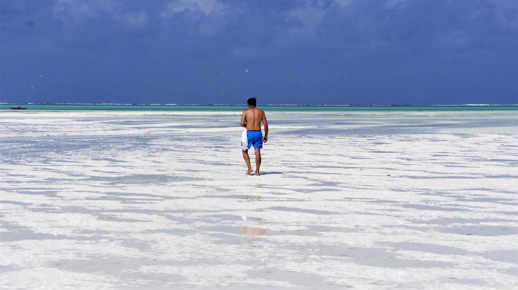 Vīrietis pastaigājas pa balto pludmali pie Reef & Beach Resort.