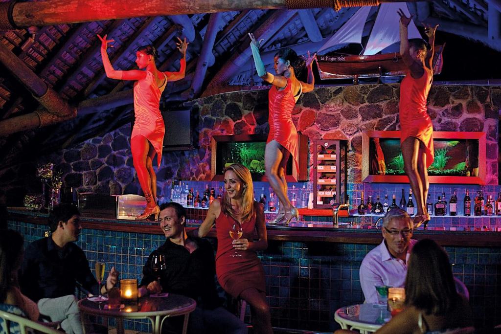 Dejotājas izpilda deju priekšnesumu bārā, kamēr viesi bauda dzērienus un izklaidi. Atmosfēra ir dzīvīga un krāsaina, radot patīkamu vakara noskaņu.