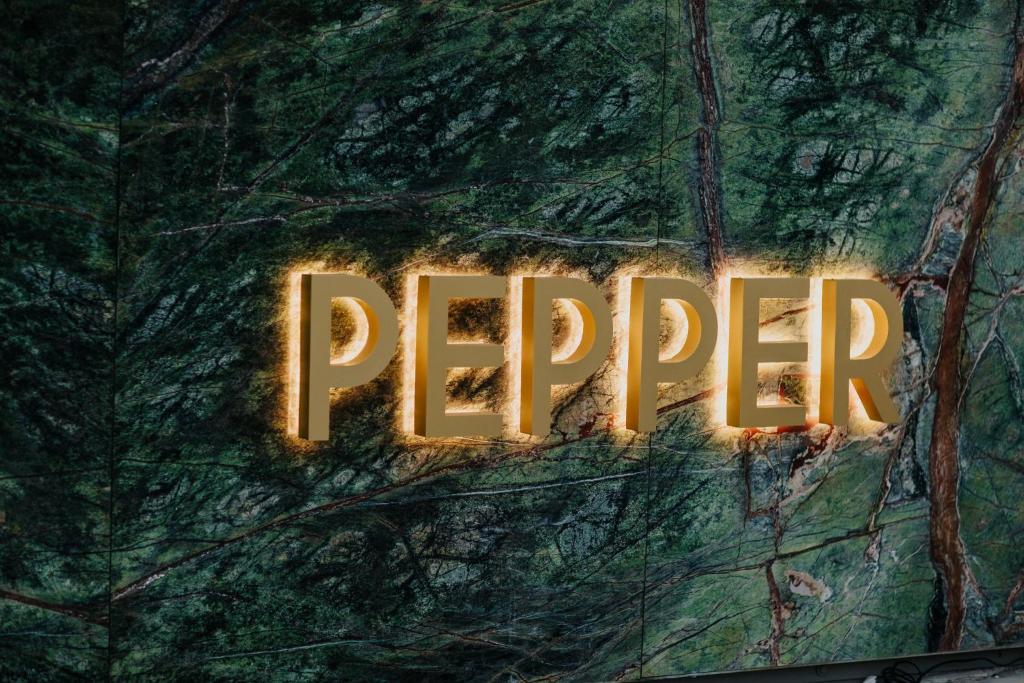 Zelta burti, kas veido vārdu "PEPPER", izceļas uz zaļā akmens fona, radot modernu un stilīgu atmosfēru.