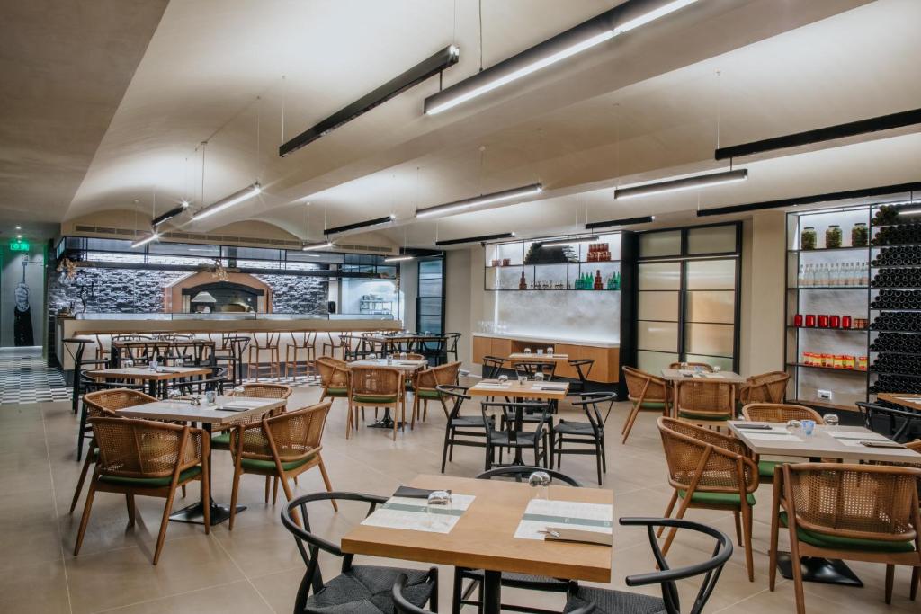 Moderns restorāns ar elegantu interjeru, kurā redzami koka galdi un krēsli, kā arī atvērta virtuve. Gaismas elementi un akmens akcenti rada patīkamu atmosfēru.
