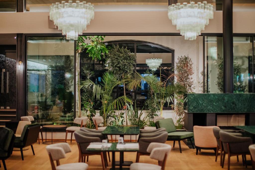 Mūsdienīga restorāna interjers ar elegantiem krēsliem, galdiem un zaļumiem. Lielas logu ailes nodrošina dabisko apgaismojumu un svaigumu.