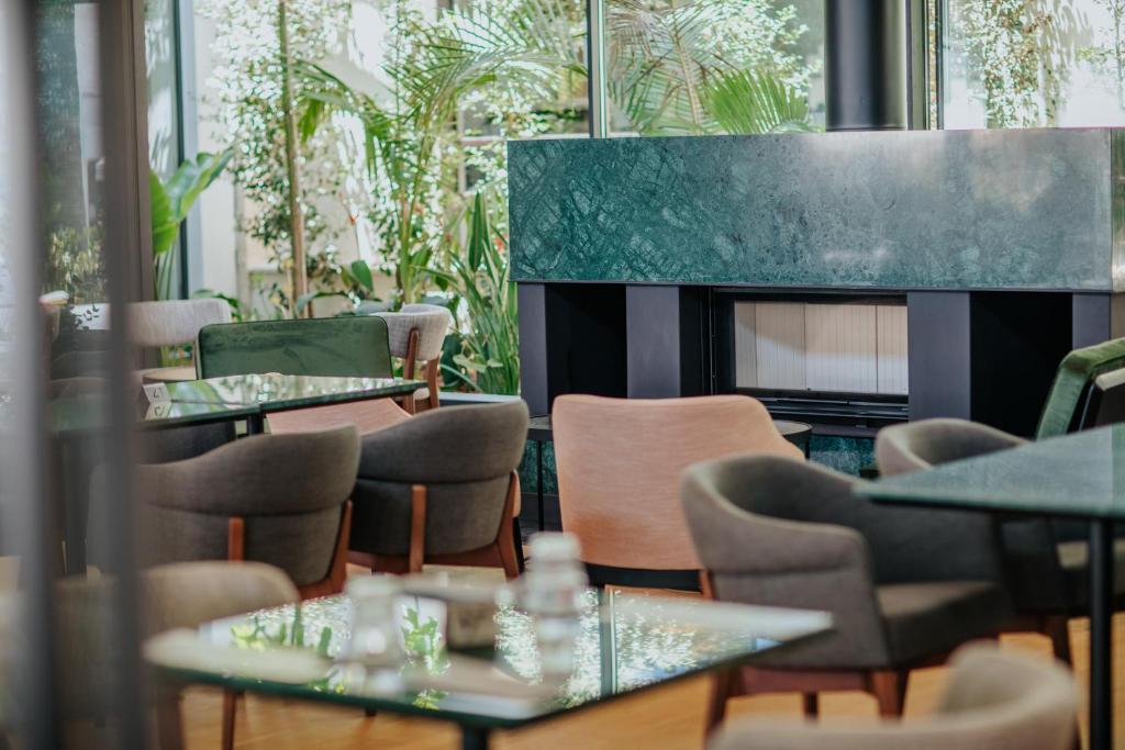 Mūsdienīgs kafejnīcu interjers ar zaļām augu dekorācijām un elegantiem krēsliem, radot relaksējošu atmosfēru.