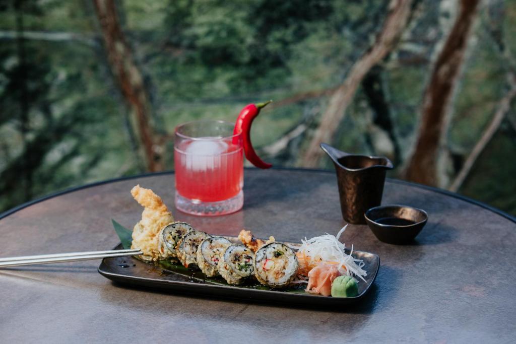Svaigs sushi ar garnelēm, dārzeņiem un garnelēm, pasniegts uz melnas šķīvja kopā ar dzērienu un sēņu mērci.