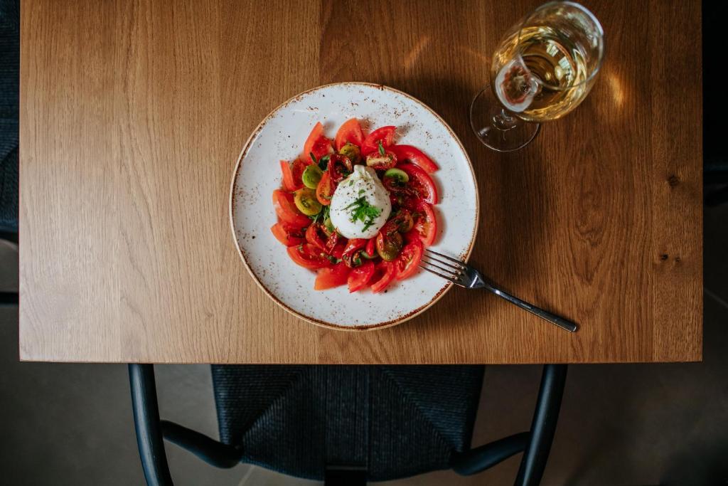 Svaiga tomātu salātu plate ar biezpiena plāksni un vīna glāzi uz koka galda.