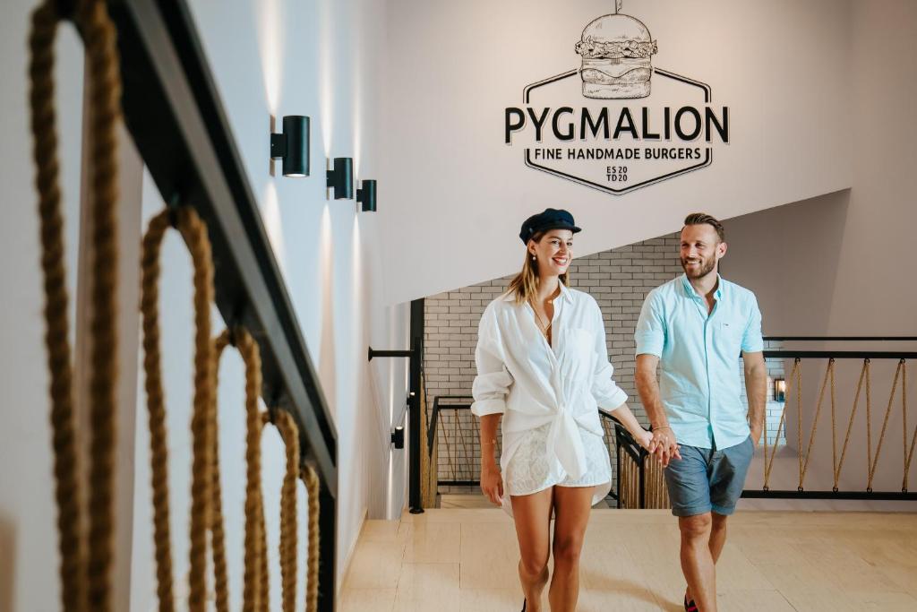 Jauna, stilīga pāris pastaigājas pa modernu restorānu ar "Pygmalion" burgeru zīmi fonā.