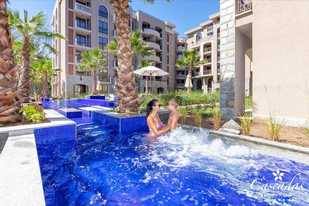 Divi cilvēki izbauda laiku baseinā, ko ieskauj palmas un moderns kūrorts. Ūdens ir spilgti zils, radot relaksējošu atmosfēru.