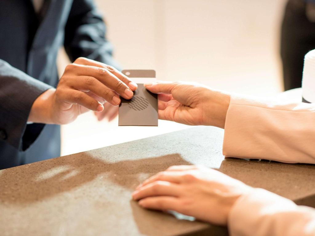 Darījums pie reģistra, kur darbinieks nodod karti klientam. Uzsvērta profesionāla apkalpošana un ērtības.