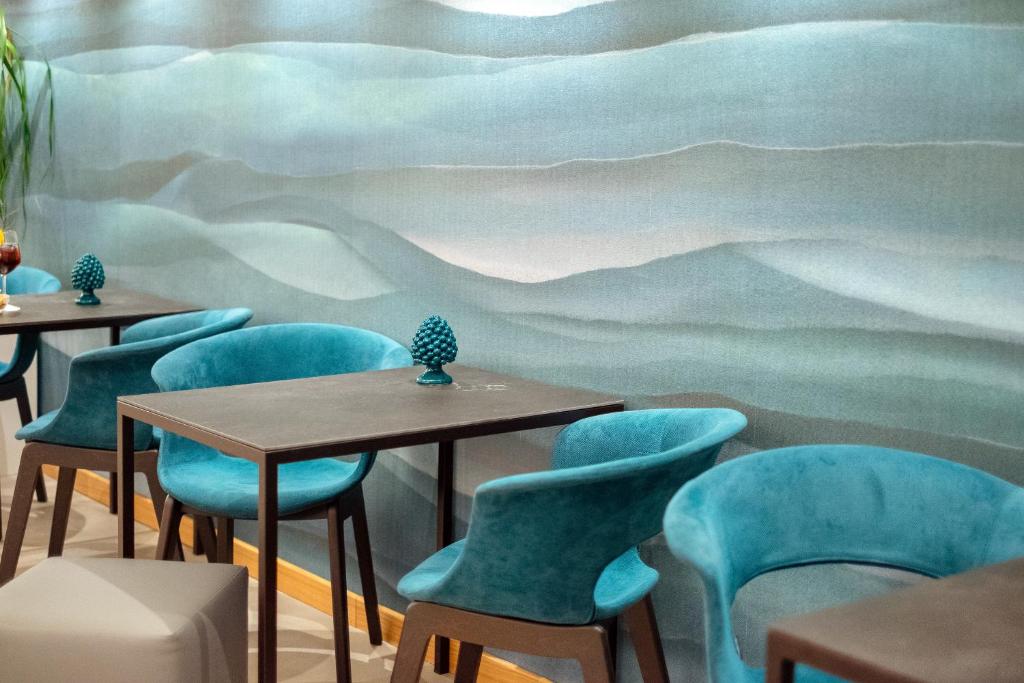 Mūsdienīgs interjers ar tirkīza krāsas krēsliem un brūniem galdiem, pretī modernai viļņveida sienai. Uz galda novietots dekoratīvs priekšmets, radot patīkamu atmosfēru.