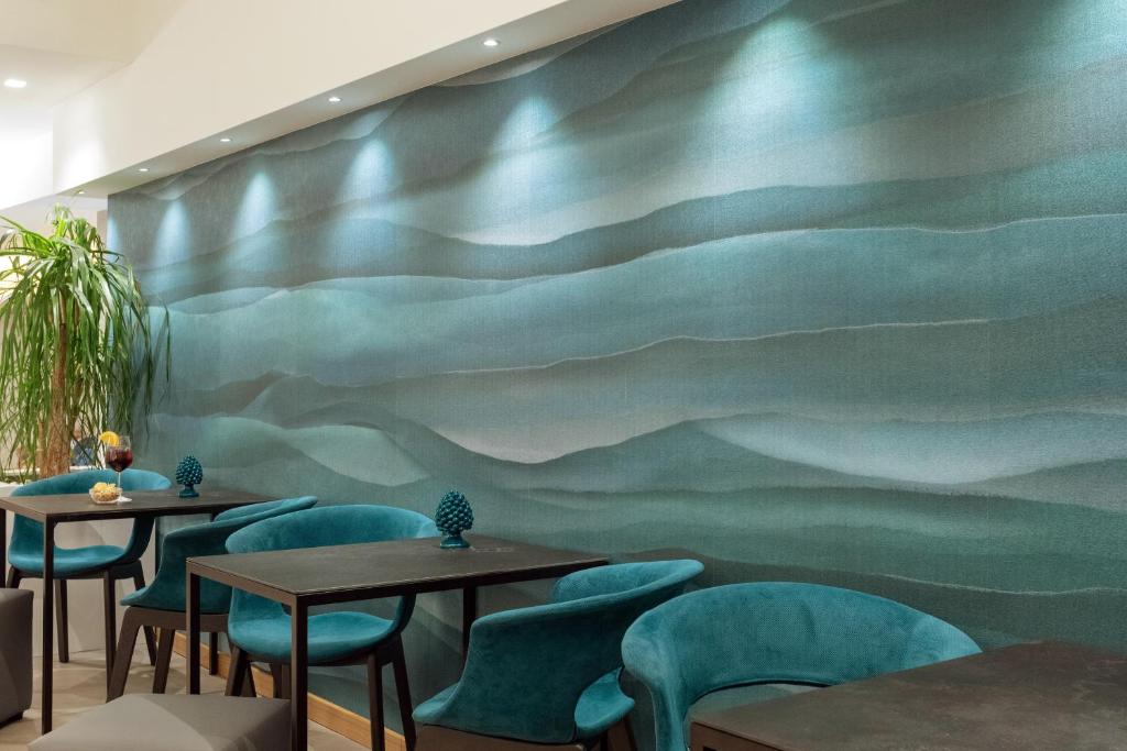 Mūsdienīga kafejnīca ar stilīgu interjeru, kurā redzama zaļgana viļņota siena un elegantas krēslu grupas.