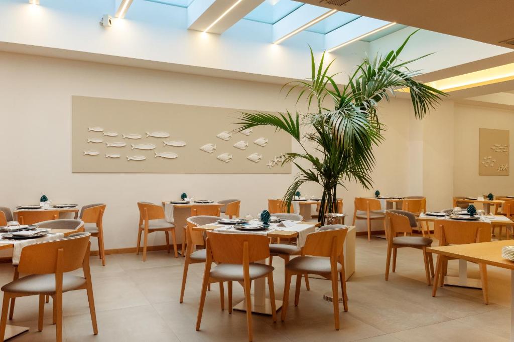Mūsdienīgs restorāns ar koka galdiem un krēsliem, kas rotāts ar palmām un mākslas darbiem uz sienām. Dabīgā gaisma ieplūst caur stikla jumtu, radot patīkamu atmosfēru.