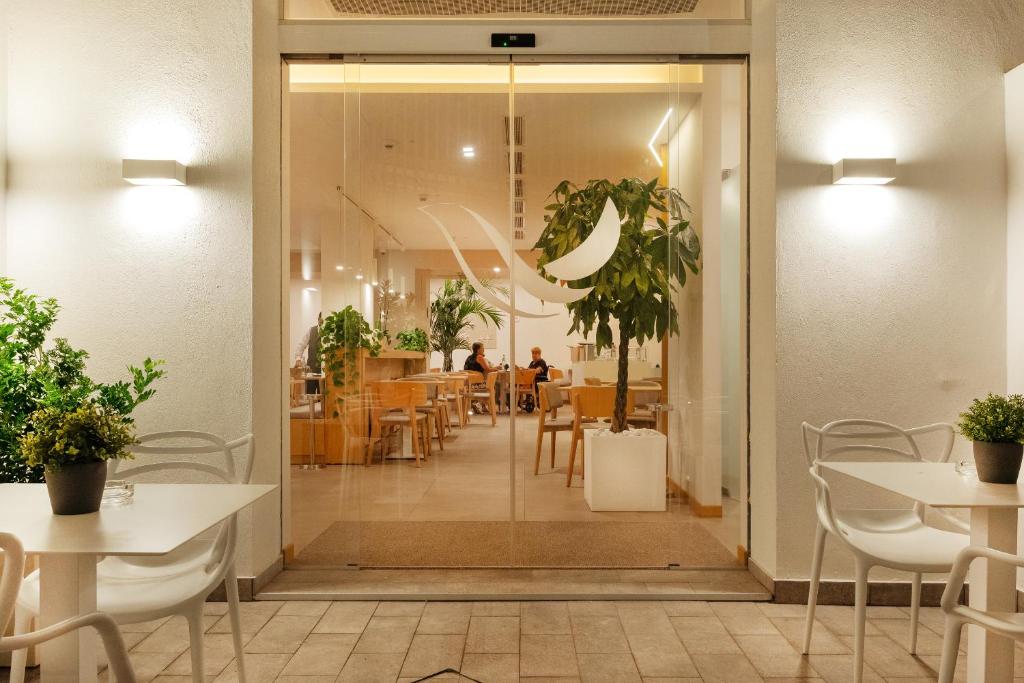 Mūsdienīga kafejnīca ar caurspīdīgām durvīm un zaļām augiem, kas rada patīkamu atmosfēru. Interjerā ir koka mēbeles un gaismas elementi, kas papildina kopējo dizainu.