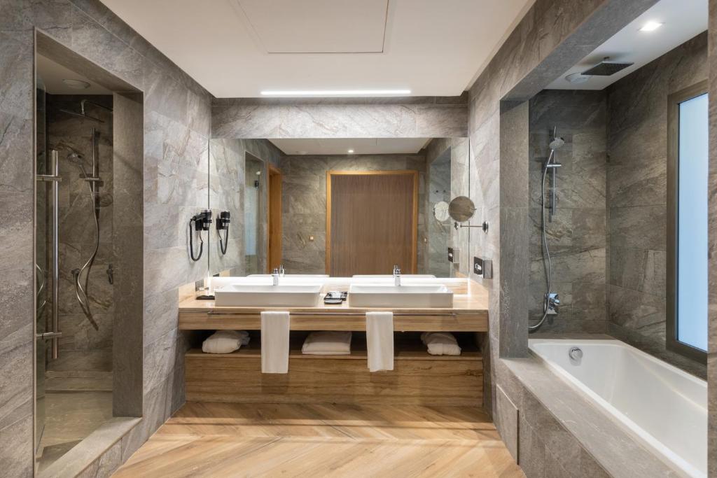 Moderns vannas istabas interjers ar divām izlietnēm, dušu un vannu, apdares materiāli no akmens un koka. Elegants un funkcionāls dizains.
