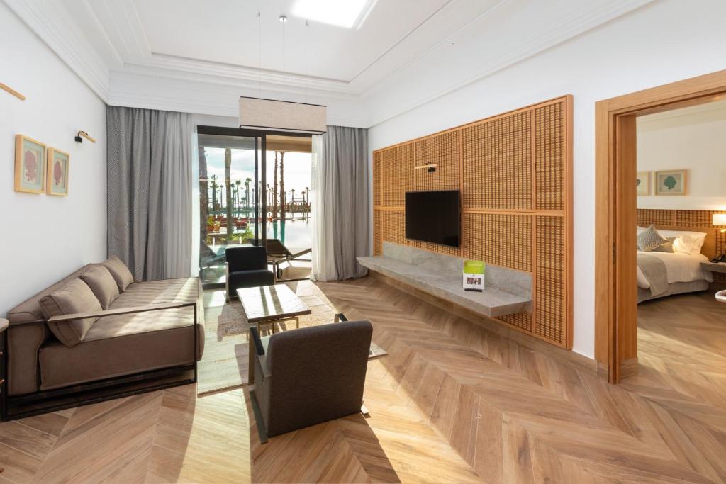 Mūsdienīgs viesnīcas numurs ar ērtu dīvānu, koka grīdu un plašām logiem, kas paver skatu uz ārējo terasi. Interjers ir elegants, ar neitrālām krāsām un minimālistisku dizainu.