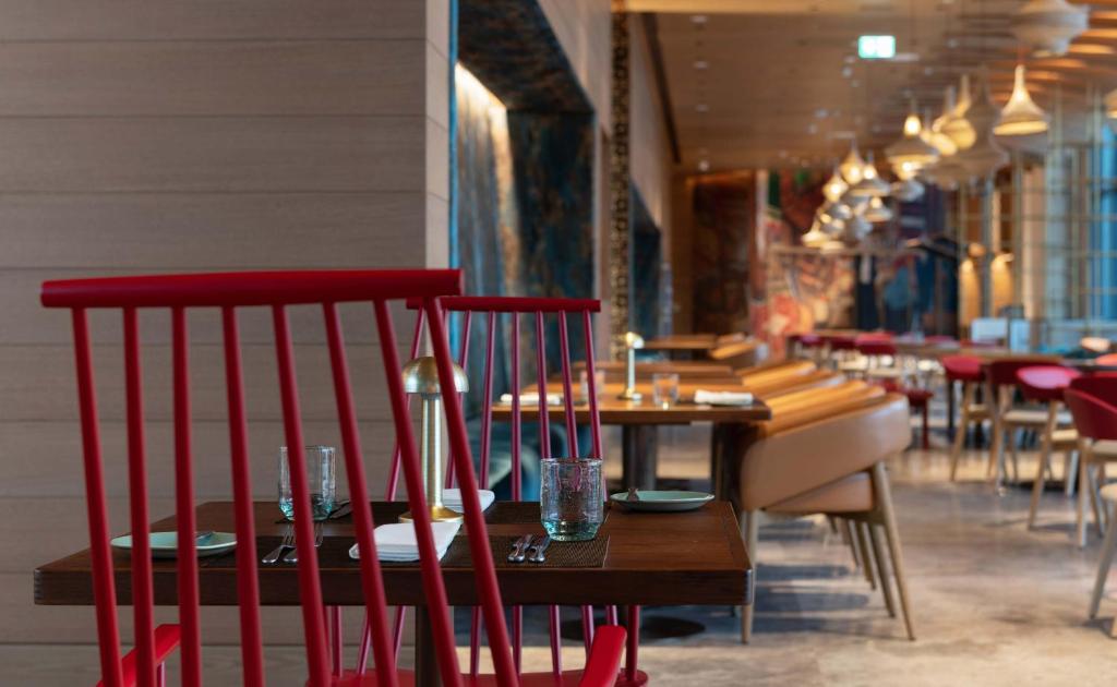 Mūsdienīgs restorāns ar stilīgu interjeru, kurā redzami sarkani krēsli un eleganta galda iestatīšana. Gaisma un dizains rada patīkamu atmosfēru.