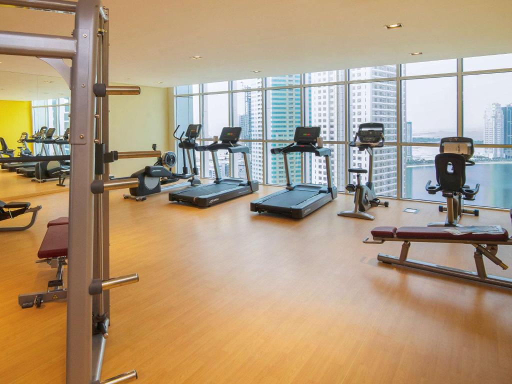Moderns sporta zāles interjers ar skatu uz pilsētu, aprīkots ar dažādām fitnesa iekārtām, tostarp skrejceliņiem un svaru trenažieriem. Ideāla vieta aktīvai atpūtai un treniņiem.