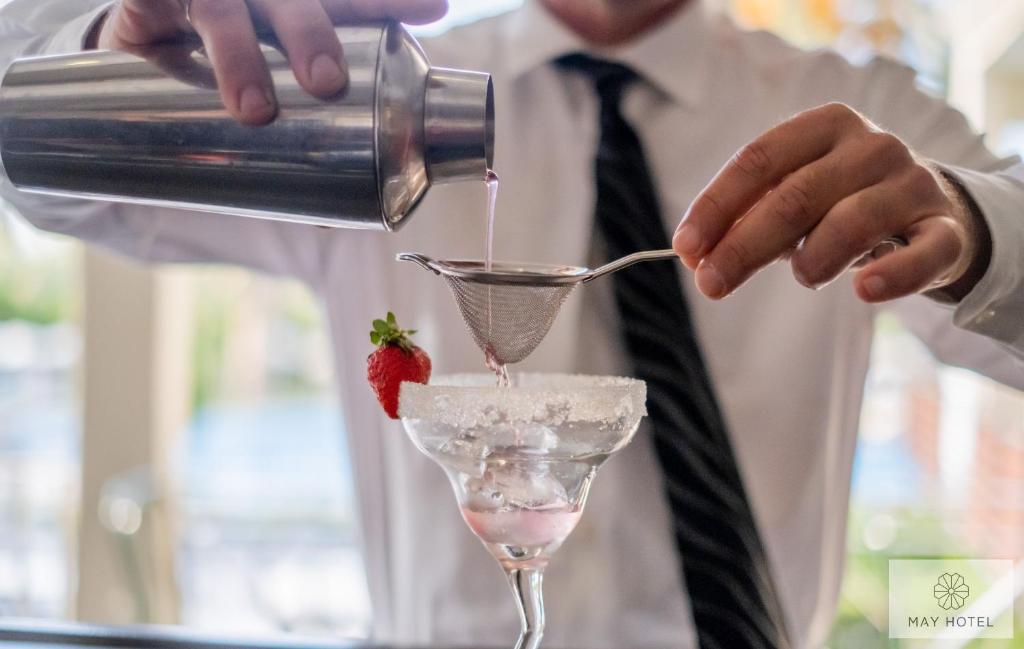 Bārmenis ielej martini kokteili caur sietiņu, dekorējot to ar zemeņu, kamēr glāze ir rotāta ar sāli.
