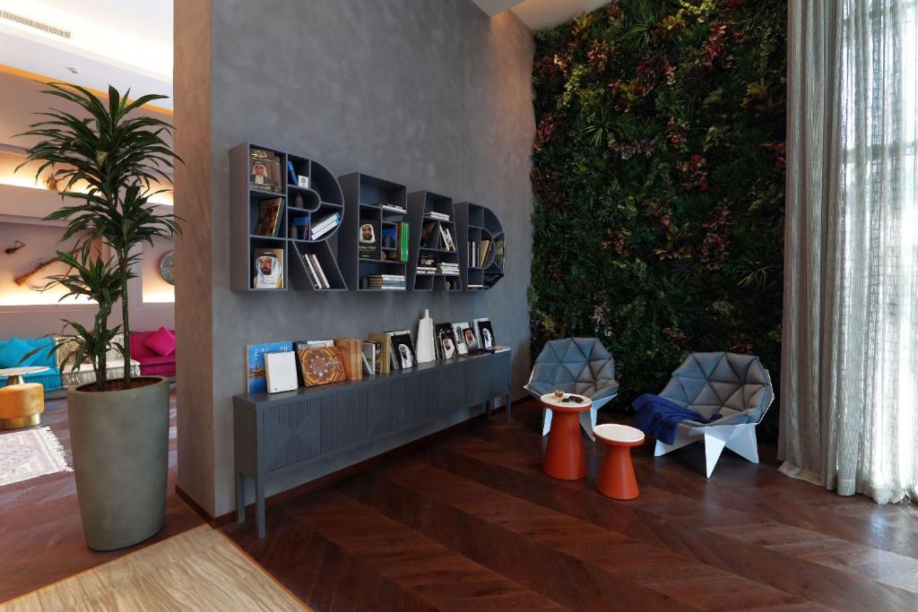 Mūsdienīga atpūtas zona ar grāmatu plauktu, kas veidots, lai veicinātu lasīšanu. Telpā ir zaļumi un stilīgas mēbeles, kas rada patīkamu atmosfēru.