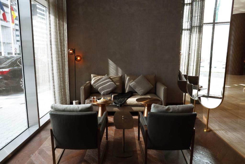 Mūsdienīgs viesnīcas interjers ar ērtu dīvānu un krēsliem, kas izveidots relaksējošai atmosfērai. Gaismas elementi un lieli logi piepilda telpu ar dabisko apgaismojumu.