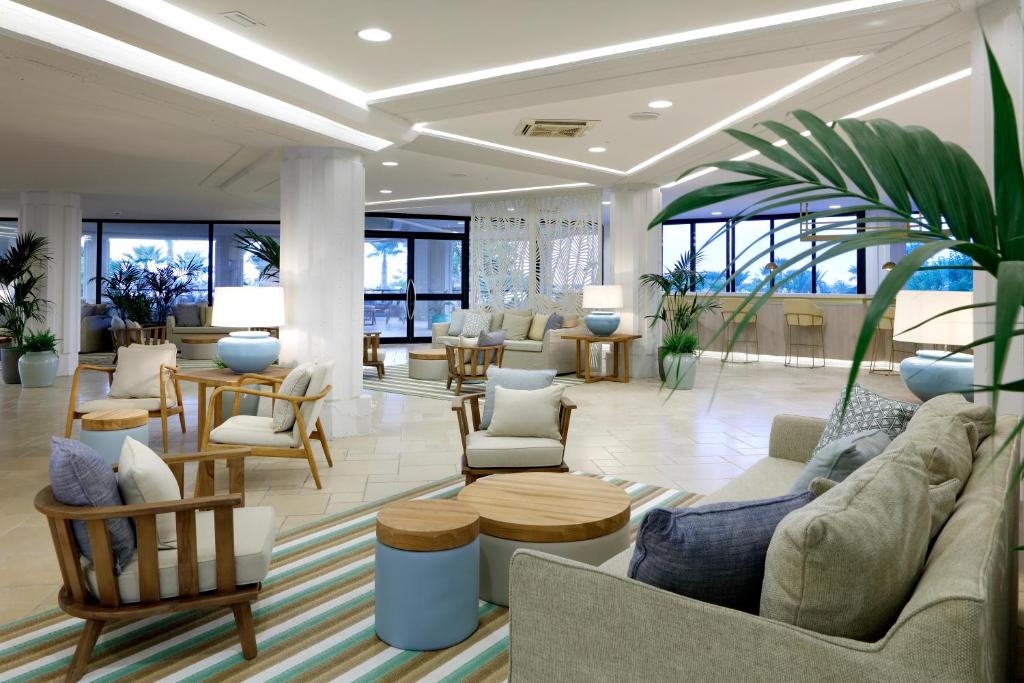 Mūsdienīgs viesnīcas interjers ar ērtām mēbelēm, zaļiem augiem un dabīgu apgaismojumu, radot relaksējošu atmosfēru. Stils apvieno modernitāti un komfortu.