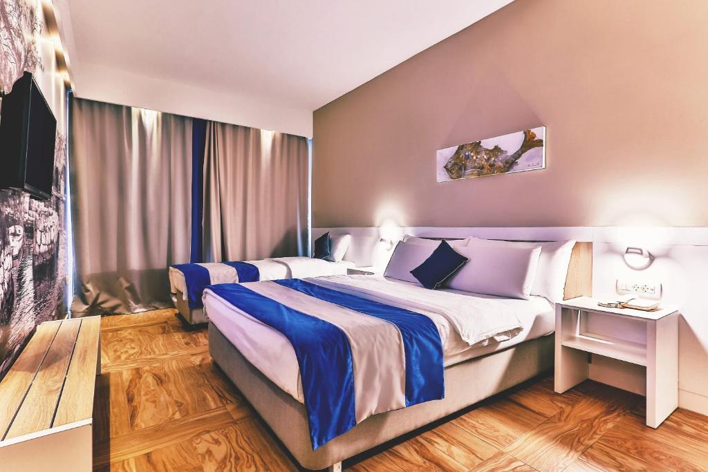 Mūsdienīgs viesnīcas numurs ar divām gultām, elegantiem interjera elementiem un mājīgu atmosfēru. Logu aizkari piešķir intimitāti, bet televizors un blakus esošā mēbele nodrošina komfortu.