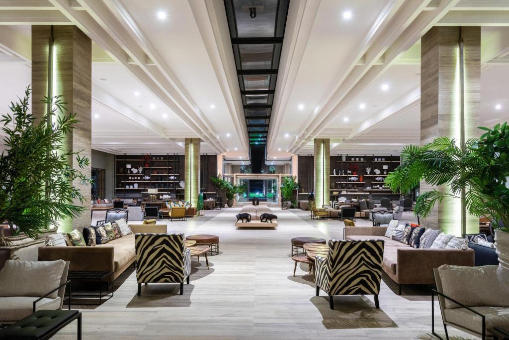 Mūsdienīgs viesnīcas vestibils ar elegantu interjeru, zaļām augu dekorācijām un komfortablām sēdvietām, radot viesmīlīgu atmosfēru.