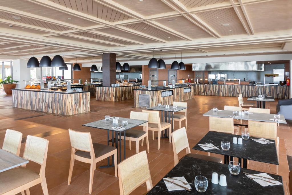 Moderns restorāns ar elegantiem galdiem un krēslām, iekārtots ar koka akcentiem un melniem lampām. Atvērta virtuve un plaša telpa rada patīkamu atmosfēru.