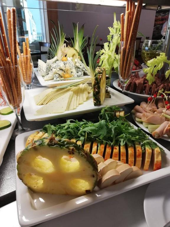 Svaigu dārzeņu un sieru bufete ar ananāsu, rukolu un krekeriem, kas izkārtoti uz baltām šķīvēm.