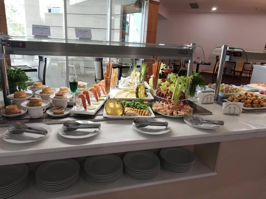 Bufete ar dažādiem ēdieniem, tostarp garnelēm, dārzeņiem un desertiem, ar galda piederumiem un paplātes uz balta galda.