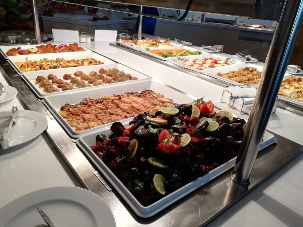 Bagātīgs bufetes galds ar dažādiem ēdieniem, tostarp jūras produktiem, gaļas ēdieniem un dārzeņiem. Uzsvars uz krāsainām prezentācijām un svaigām sastāvdaļām.