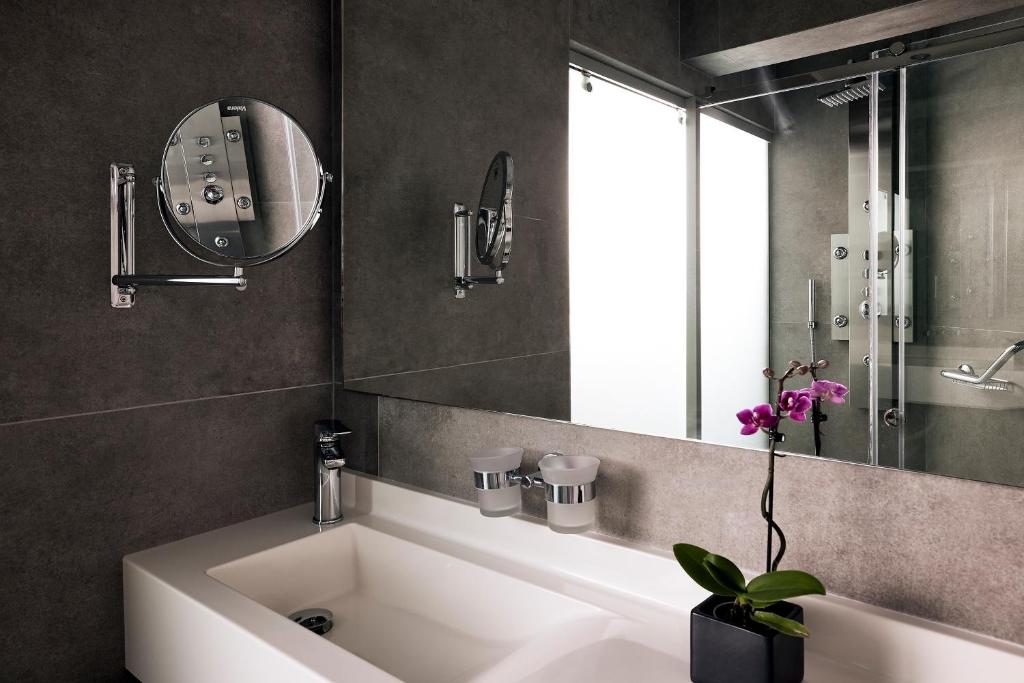 Moderna vannas istaba ar elegantu spoguli un orhideju uz izlietnes. Rūpīgi izvēlēti materiāli un apgaismojums rada patīkamu atmosfēru.