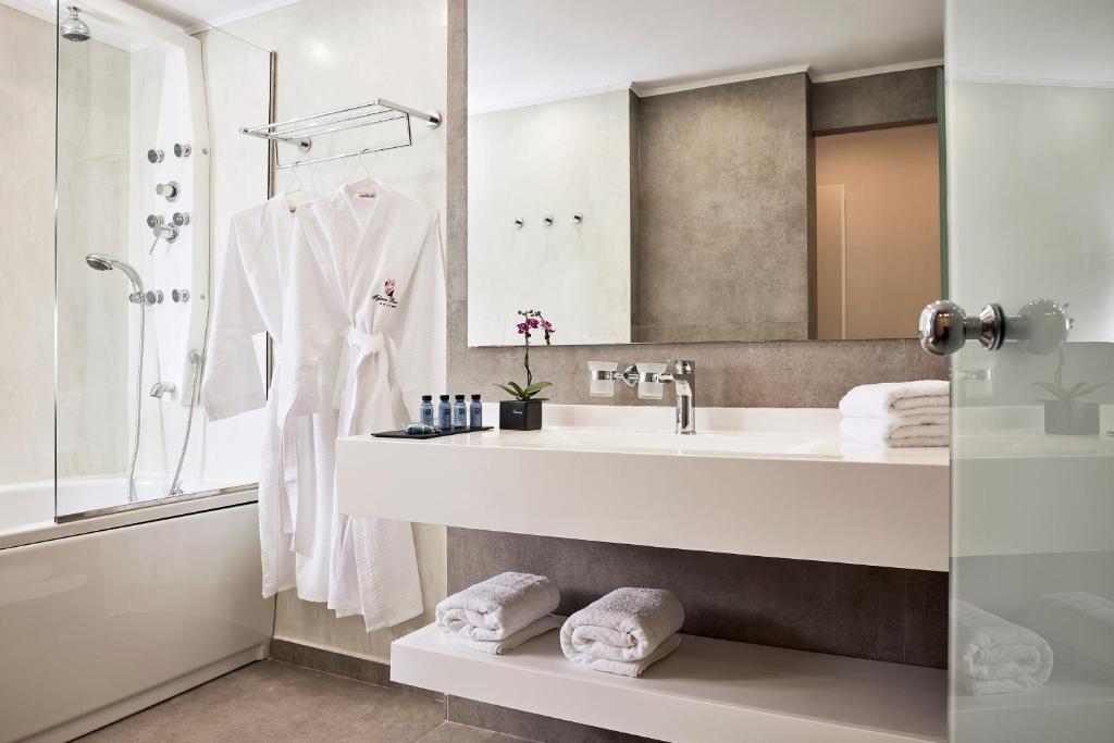 Mūsdienīgs vannas istabas interjers ar stikla dušu, baltām dvieļiem un halātiem, kā arī dekoratīvu augu un higiēnas līdzekļiem. Stilīgs un elegants dizains rada relaksējošu atmosfēru.