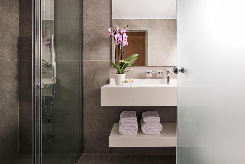 Moderns vannas istabas interjers ar stikla dušu, elegantu izlietni un orhideju pušķi, kas piešķir telpai svaigumu. Balti dvieļi ir salocīti uz plaukta, radot patīkamu atmosfēru.