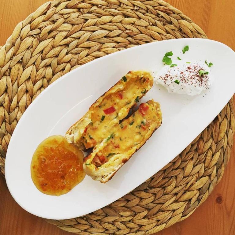 Svaigs dārzeņu omlete ar sieru, pasniegta ar garšvielām un saldā mērce, uz baltas šķīvja.