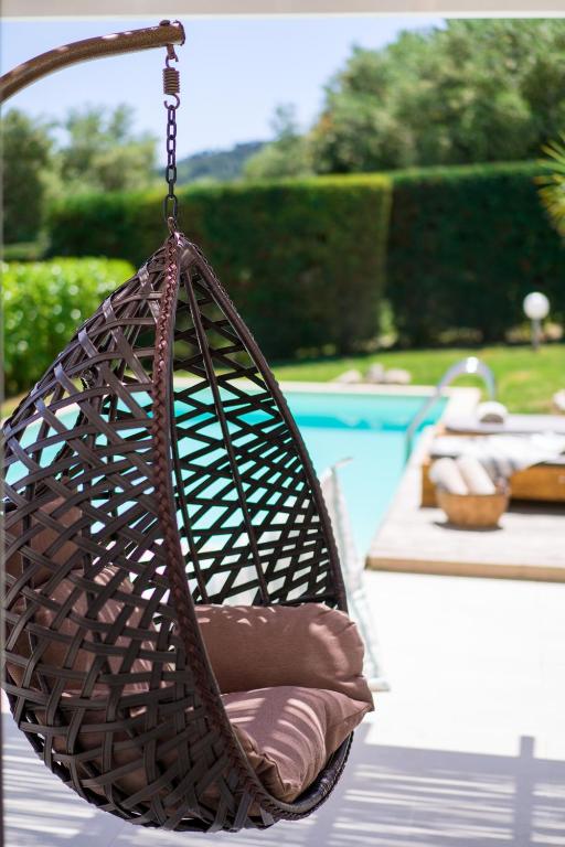 Atsāls šūpuļkrēsls ar spilvenu, kas karājas pie baseina, veido relaksējošu atmosfēru dārzā. Fonā redzams zaļš zāles laukums un baseins.