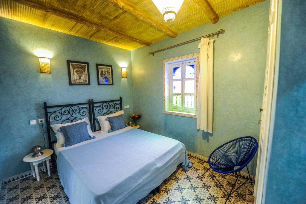 Mūsdienīgs guļamistabas interjers ar divguļamo gultu, zilu sienu krāsu un dekoratīviem apgaismojuma elementiem. Telpā ir stilīga mēbeļu izvēle un logi ar krāsainām stikla detaļām.