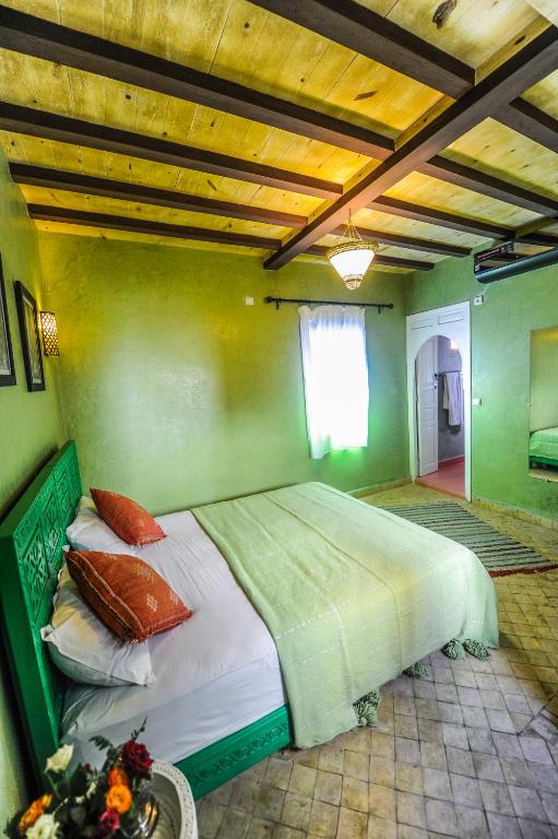 Mūsdienīgs guļamistabas interjers ar zaļām sienām, koka griestiem un ērtiem gultas piederumiem, radot relaksējošu atmosfēru. Interjerā ir iekļauti dekoratīvi elementi un dabiska apgaismojuma avoti.