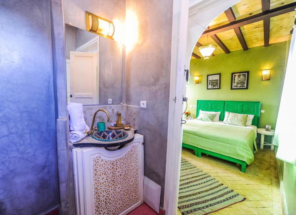 Mūsdienīga viesnīcas numura interjers ar zaļām gultām un dekoratīvu vannas istabu, kas izceļs ar elegantu apgaismojumu un tradicionālām detaļām.