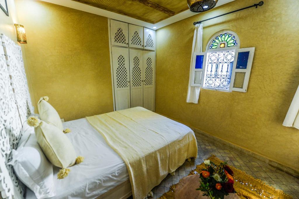 Mūsdienīga guļamistaba ar dzeltenām sienām, elegantu gultu un dekoratīvām akcentiem, kas rada siltu un viesmīlīgu atmosfēru. Logā ir krāsaini stikli, kas piešķir telpai unikālu raksturu.