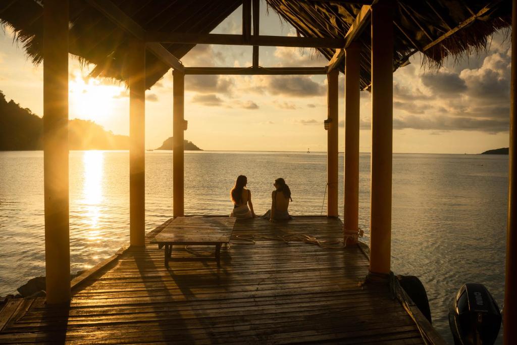 Divi cilvēki sēž uz piestātnes pie saulrieta The Aiyapura Koh Chang Resort