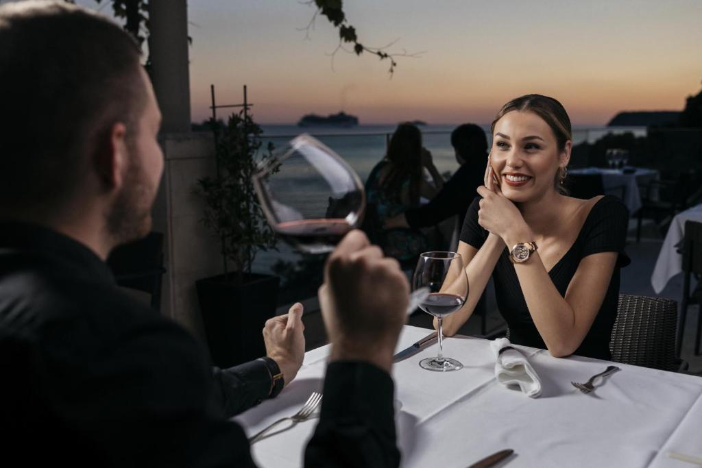 Romantiska vakariņas pie jūras saulrieta laikā, kur pāris bauda vīnu un viens otra kompāniju elegantā restorānā.