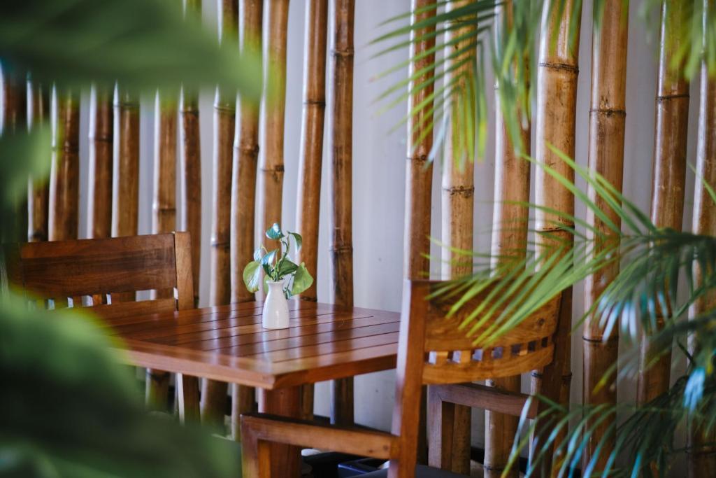 Koka galds ar krēslu un nelielu vāzi ar ziediem, fona bambusa siena un zaļiem augiem.