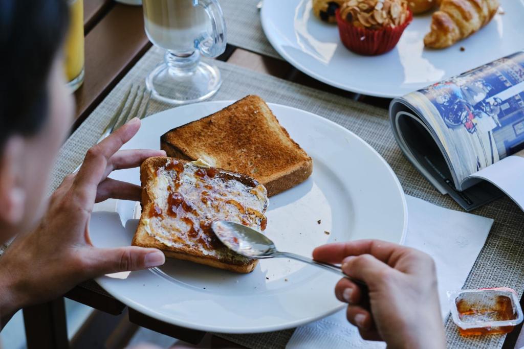 Svaigas maize ar ievārījumu un sviestu, kas tiek pasniegta brokastīs, blakus ir krūze ar kafiju un dažādi konditorejas izstrādājumi.