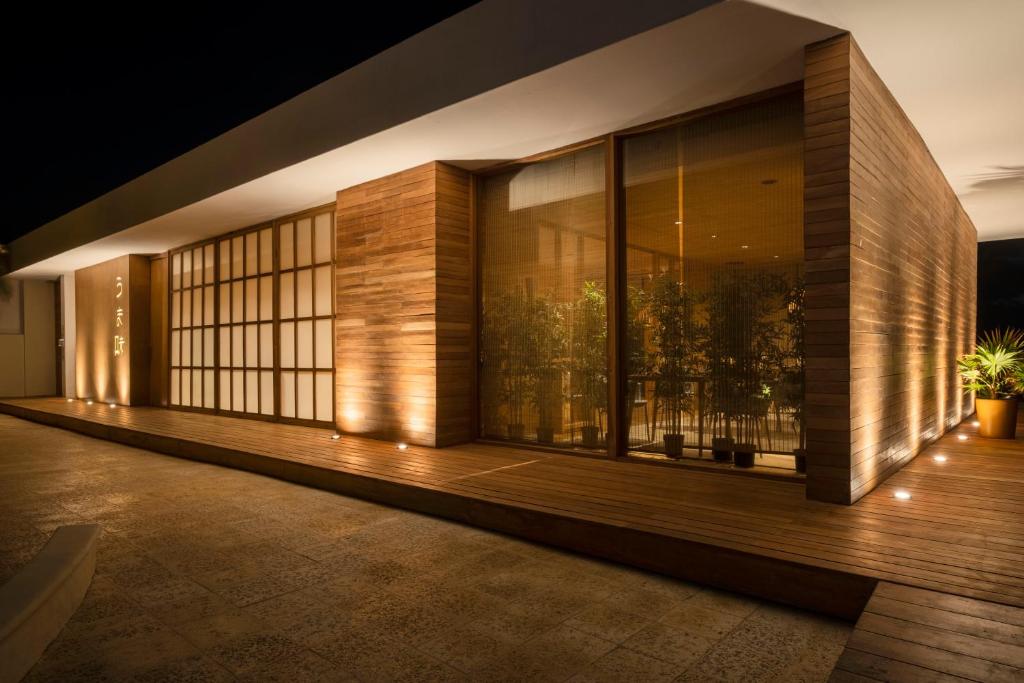 Mūsdienīgas ēkas eksterjers ar koka elementiem un apgaismojumu, kas rada siltu un aicinošu atmosfēru naktī. Apzaļumotie stūri un plašās logu virsmas nodrošina harmonisku saikni ar dabu.