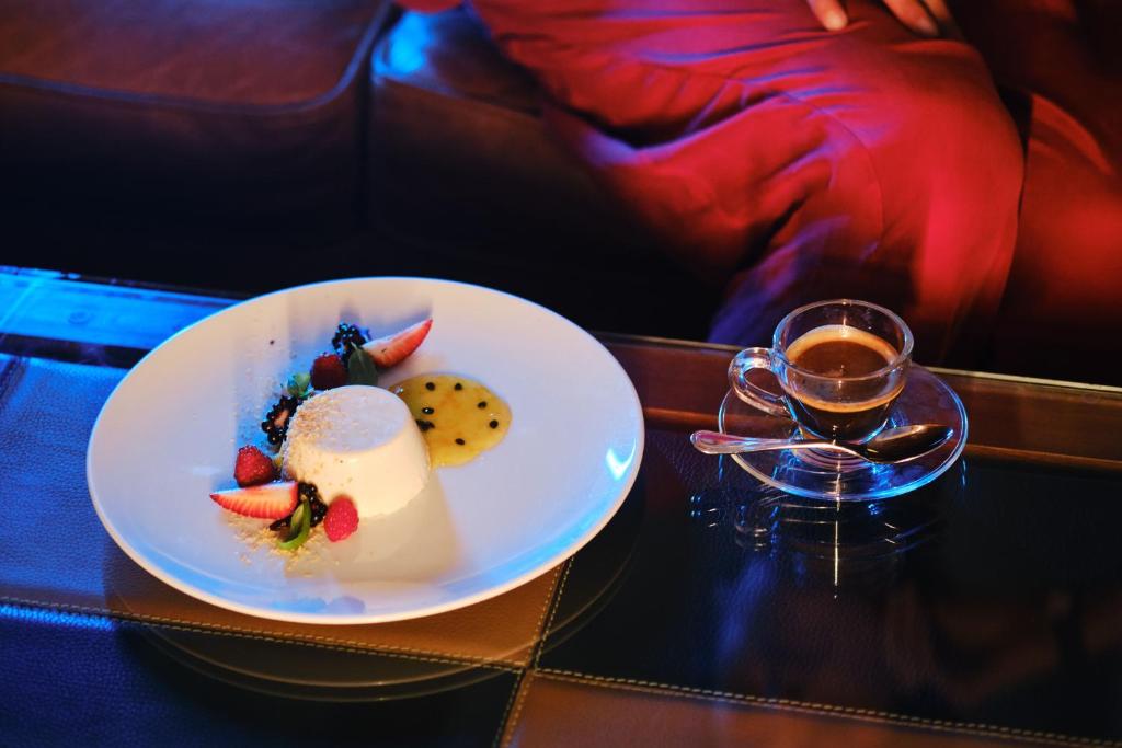 Deserta šķīvis ar krēmīgu panna cotta, dekorēts ar ogām un augļu mērci, blakus tase kafijas.