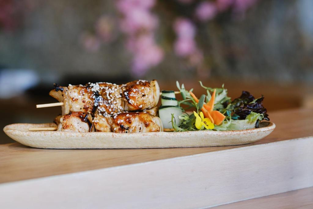 Garšīga grilēta gaļa uz kociņa, pasniegta ar svaigiem dārzeņiem un ziediem uz elegantas šķīvja. Ideāls ēdiens, lai izbaudītu gardas maltītes.