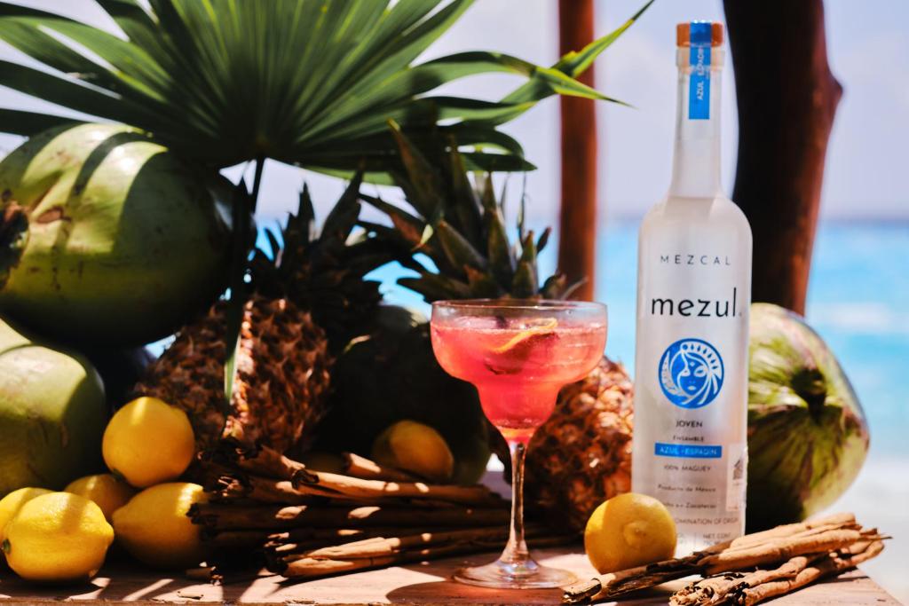Svaiga kokteiļa bilde ar mezcal pudeli un tropiskiem augļiem, piemēram, ananāsiem un kokosriekstiem, kas izveido burvīgu pludmales atmosfēru.