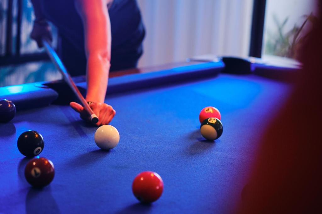 Boulings spēles brīdis ar balto bumbu un vairākām citām uz zaļā galda. Fons apgaismots ar zilu gaismu, radot dinamisku atmosfēru.